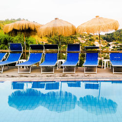 Lounge chairs by swimming pool against sky