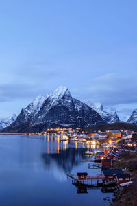 Illuminated buildings by sea against sky at dusk