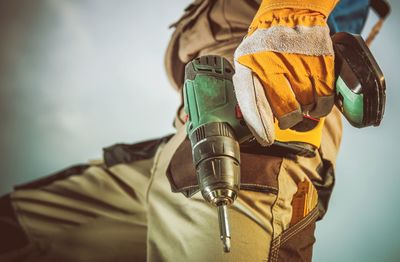 Midsection of manual worker holding drill