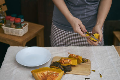 Midsection of woman cutting pumpkin at table