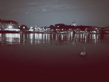 Illuminated city by sea against sky at night