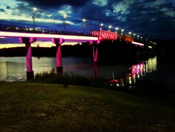 Illuminated bridge over river against cloudy sky