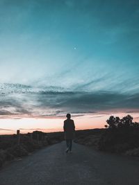 Rear view of man walking on street against sky during sunset