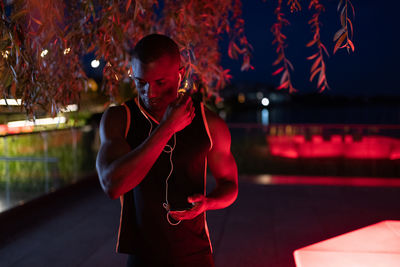 Ethnic athlete putting on earphones at night