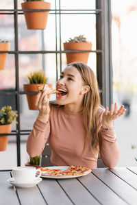 Funny european woman with a sweet smile eats pizza on the terrace of a summer cafe