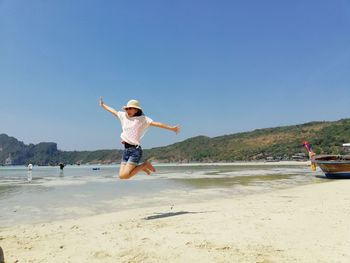 Portrait of woman with arms outstretched jumping at beach