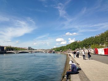 People on bridge over river in city against sky