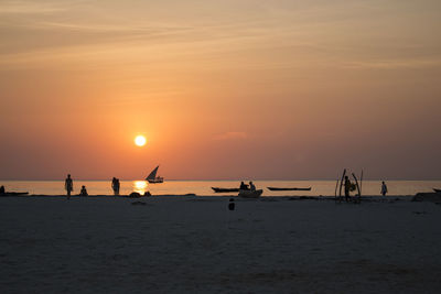 Silhouette people at beach against sky during sunset