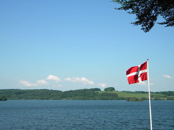 Danish flag by sea against blue sky