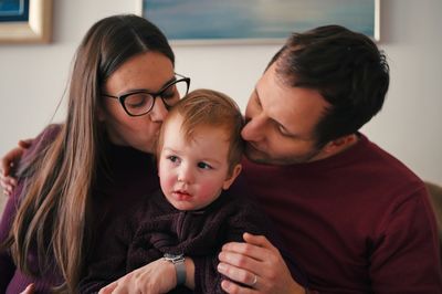 Parents and their little toddler sitting on a sofa and watching tele vision