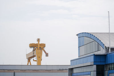 Low angle view of crane by building against sky