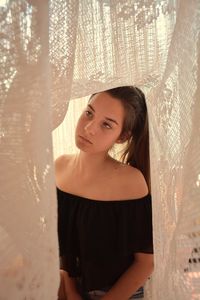 Thoughtful young woman standing amidst curtain