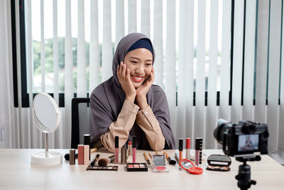 Young woman blogging while applying make up at office