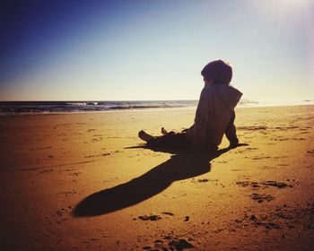 Boy sitting on sand against sea at beach
