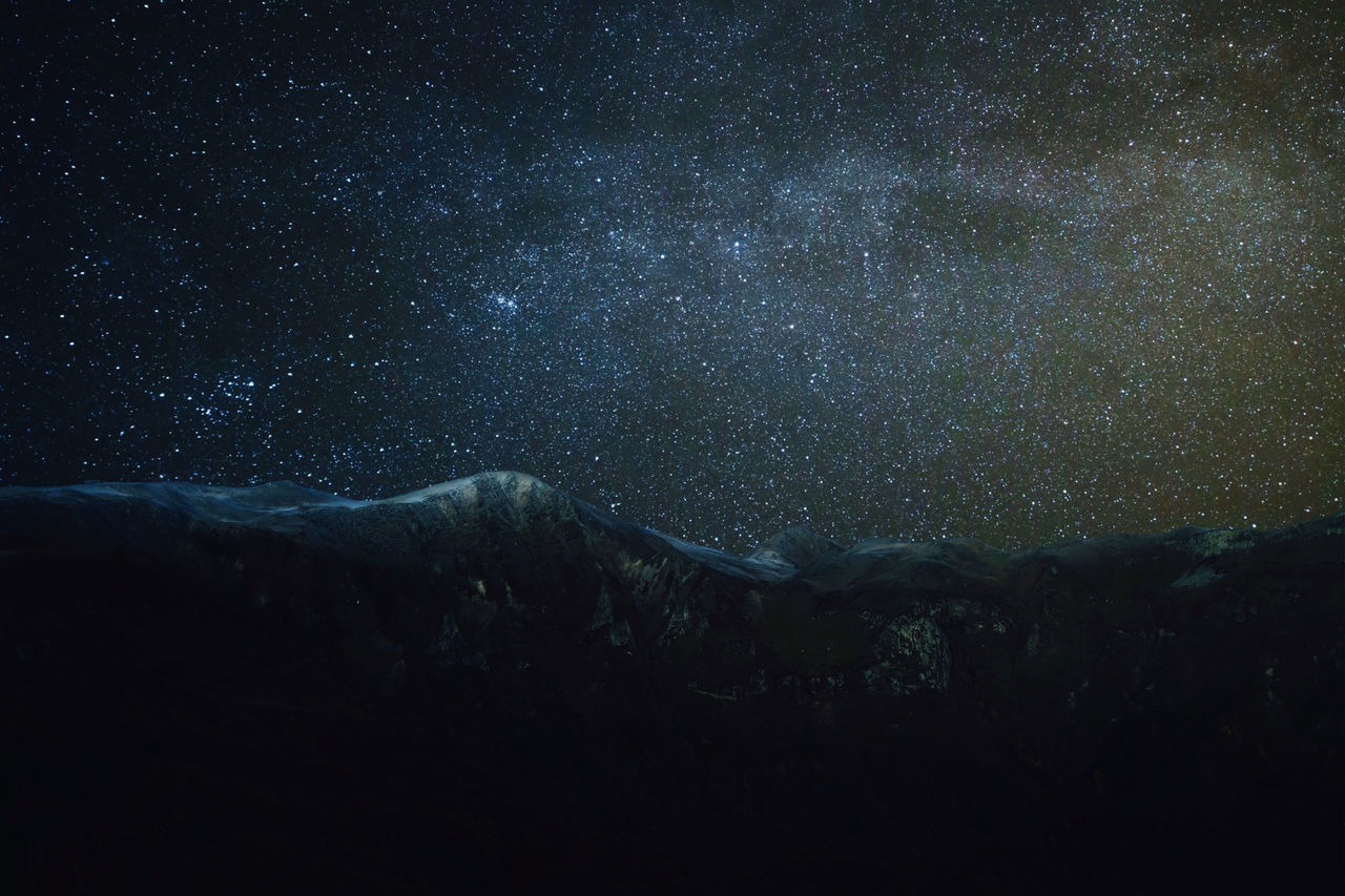 LOW ANGLE VIEW OF MOUNTAIN AGAINST STAR FIELD AT NIGHT