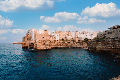 Buildings by sea against cloudy sky