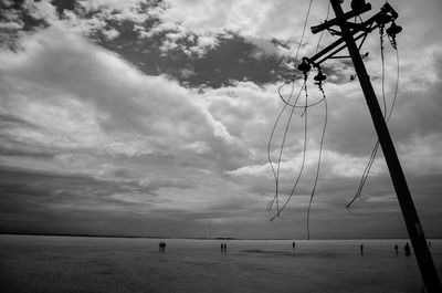 Damaged electricity pylon by lake against cloudy sky