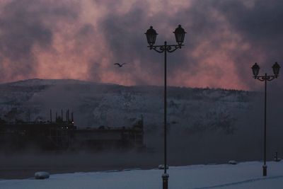 Street light on snow covered field against sky at dusk