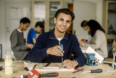 Portrait of smiling male teenage student with screwdriver during carpentry class