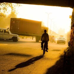 Man cycling on street with cars and trucks in background