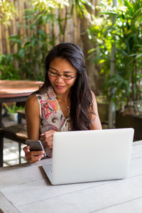 Young woman using mobile phone while sitting on table