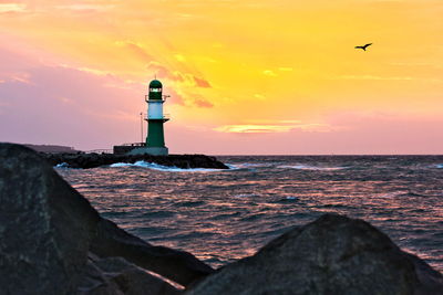 Lighthouse by sea against sky during sunset