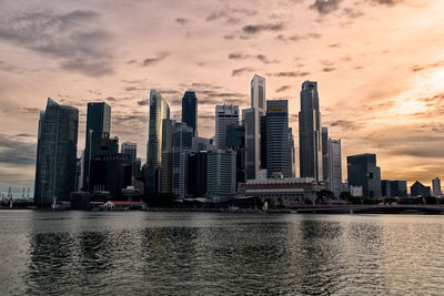 Cityscape at waterfront against cloudy sky