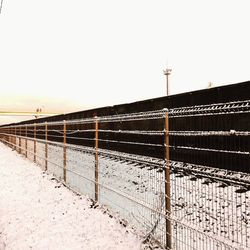 Fence on snow covered landscape against clear sky