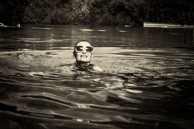 A vintage photo of a woman in a black swimsuit and white sunglasses swimming in the pool