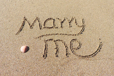 Marry me text on wet sand at beach