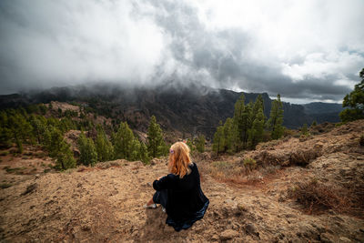 Rear view of woman sitting on mountain against sky