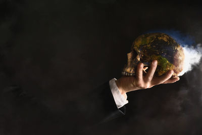 Close-up of hand holding skull with smoke against black background