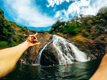 Midsection of person by waterfall against trees