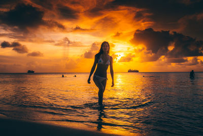 Silhouette woman standing at beach against sky during sunset