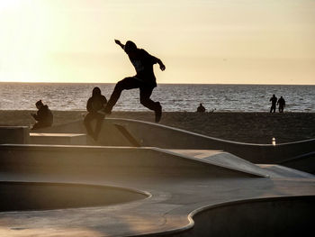 Silhouette people jumping on beach against sky during sunset