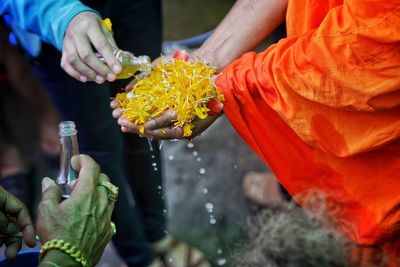 Low section of person pouring liquid on monk hands outdoors