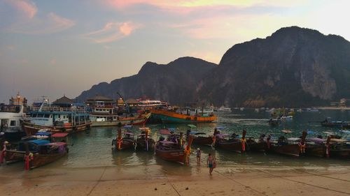 Longtail boats moored at harbor against sky during sunset