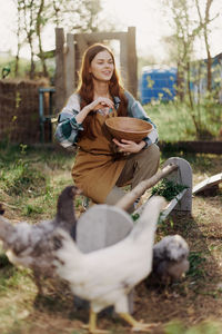 Happy female farmer feeding chickens at farm