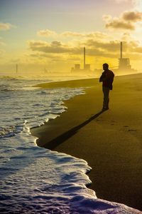 Silhouette man standing on beach against sky during sunset