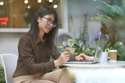 Young woman using mobile phone while sitting on table