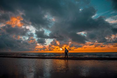 Man standing at beach against sky during sunset