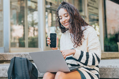 Young woman with smart phone using laptop outdoors