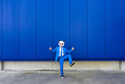 Full length portrait of teenage girl standing against blue wall