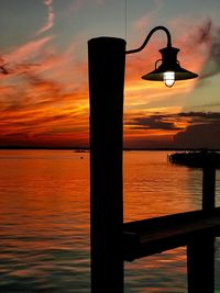 Silhouette street light by sea against orange sky