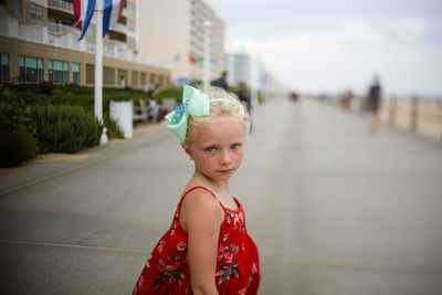 Little girl in red dress on boardwalk big bow serious expression