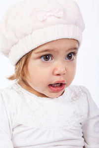 Close-up of cute baby girl looking away while wearing hat against white background