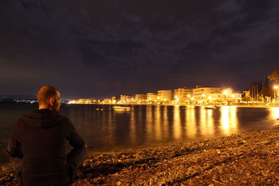 Rear view of woman standing at illuminated city against sky at night