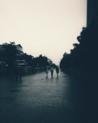 People walking on footpath in city against clear sky