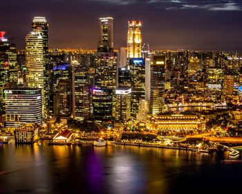 Illuminated buildings by river against sky at night