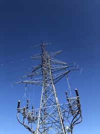 Low angle view of electricity pylon against blue sky